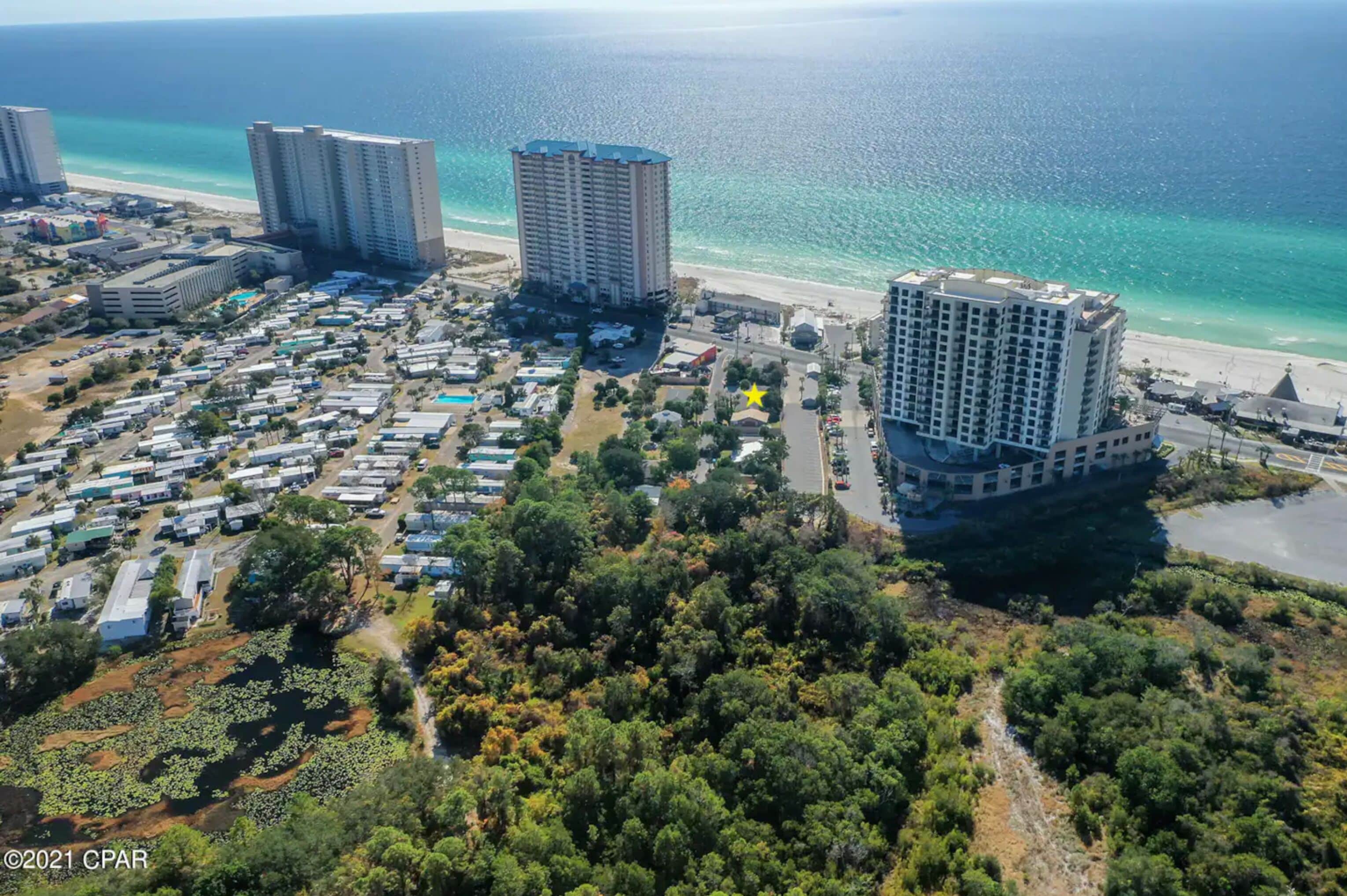 Vista aérea de una zona turística costera con varios edificios de gran altura, una playa y un conjunto denso de construcciones más pequeñas.