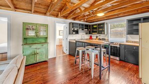 A kitchen with wooden beams, a green cabinet, bar stools, and modern appliances. - Young Street Homes (Panama City Beach)