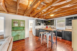 A kitchen with wooden beams, a green cabinet, bar stools, and modern appliances. - Young Street Homes (Panama City Beach)