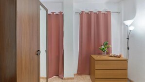 Una habitación con un armario de madera, un aparador de madera, una lámpara y cortinas rosadas.