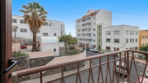 Un balcón con vista a una calle, una palmera y edificios modernos.