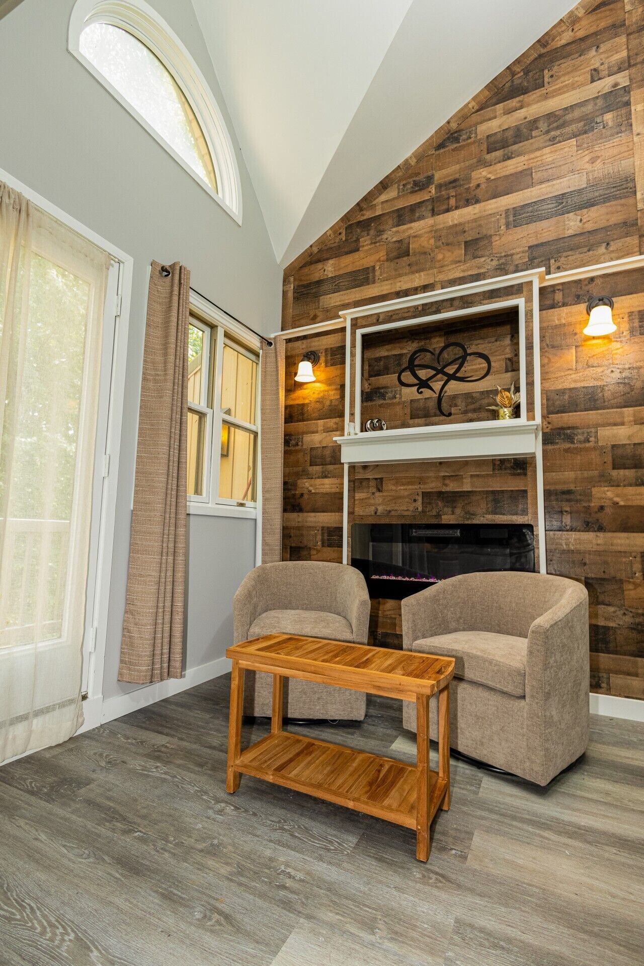 A room with a fireplace, two armchairs, a wooden coffee table, and a large window with curtains.