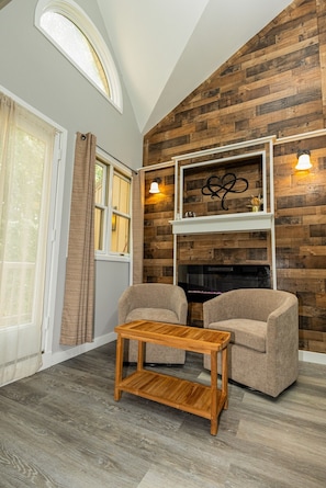 A room with a fireplace, two armchairs, a wooden coffee table, and a large window with curtains. - Pocono Mountains Escape - 2 Bedroom, 2.5 Bath, private townhome with wood-burning fireplace (East Stroudsburg)