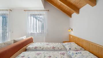 Ein Schlafzimmer mit zwei Betten, einer Holzbalkendecke und einem Fenster mit durchsichtigen Vorhängen.