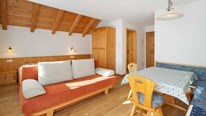 Una habitación acogedora con techo de madera, un sofá, una mesa de comedor con sillas y una puerta de madera.