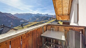 Un balcón con barandilla de madera, una mesa y una silla, con vistas a un paisaje montañoso.