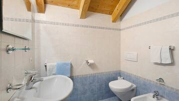 A bathroom with a sink, toilet, bidet, and mirror.