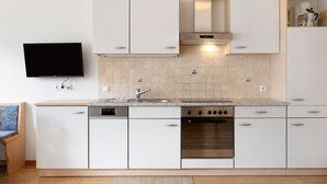 Una cocina moderna con armarios blancos, horno empotrado y un televisor de pantalla plana en la pared.