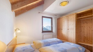 Habitación con dos camas, armario de madera, ventana con vista a la montaña y una lámpara en el techo.