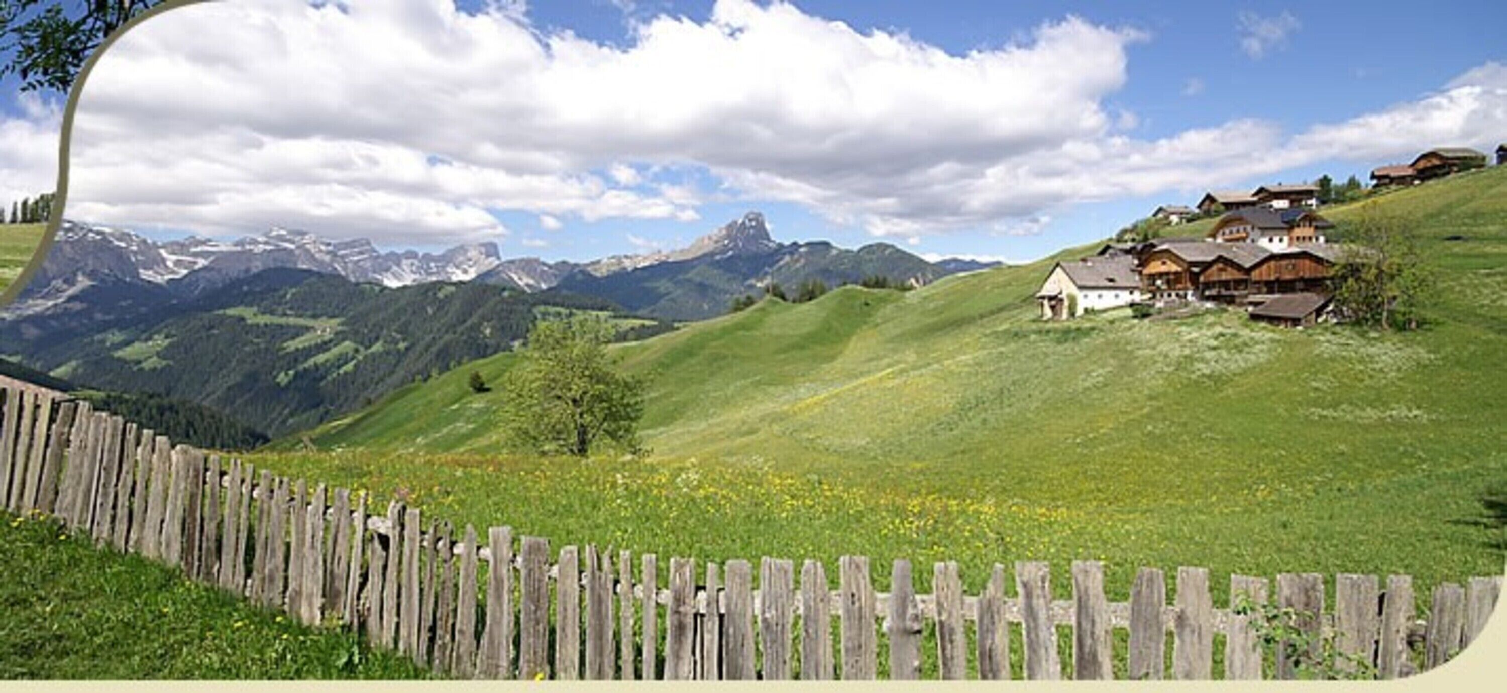 Paisaje rural con una valla de madera, campos verdes y casas tradicionales en una ladera.