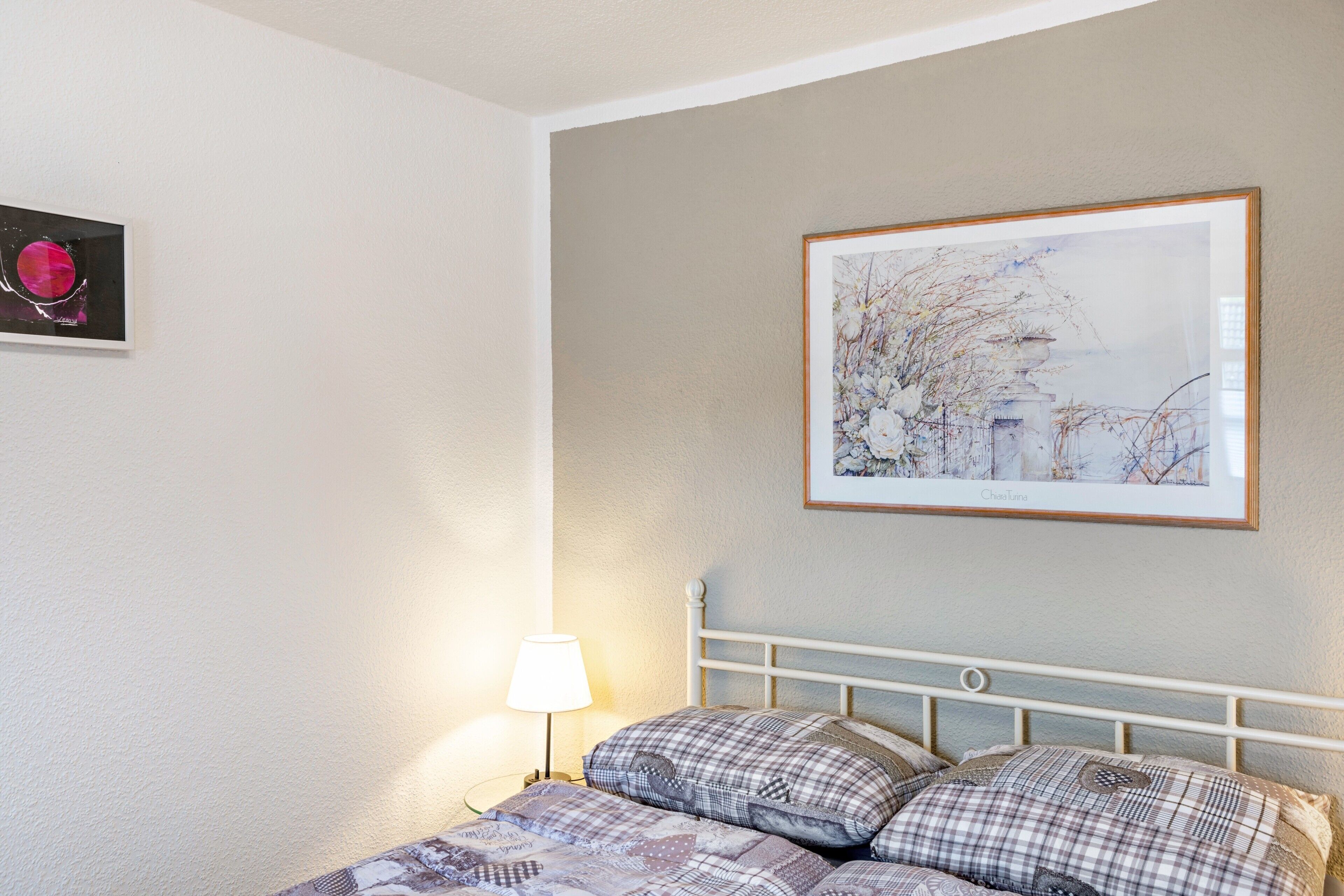 Un dormitorio con una cama, una mesita de noche, una lámpara y dos cuadros en la pared.
