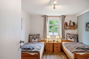 Une chambre avec deux lits en bois, une fenêtre avec des rideaux, une table de chevet avec des lampes et une bibliothèque contenant des livres et des objets décoratifs.