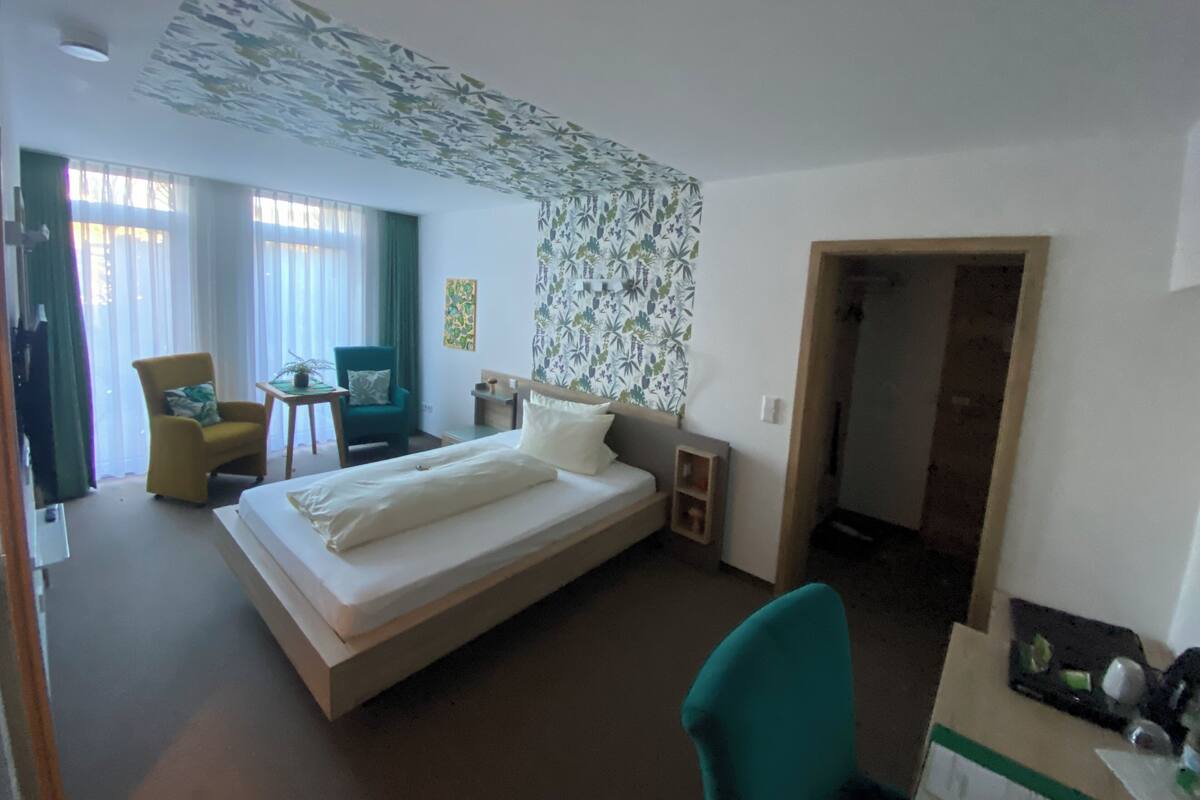 A hotel room with a bed, a desk, a chair, a small table, and a window with curtains.