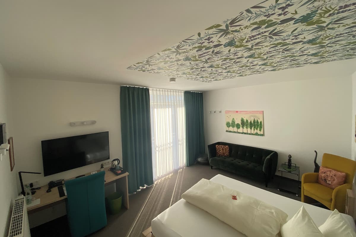 A hotel room with a bed, a TV, a desk with a computer, a sofa, and a chair.