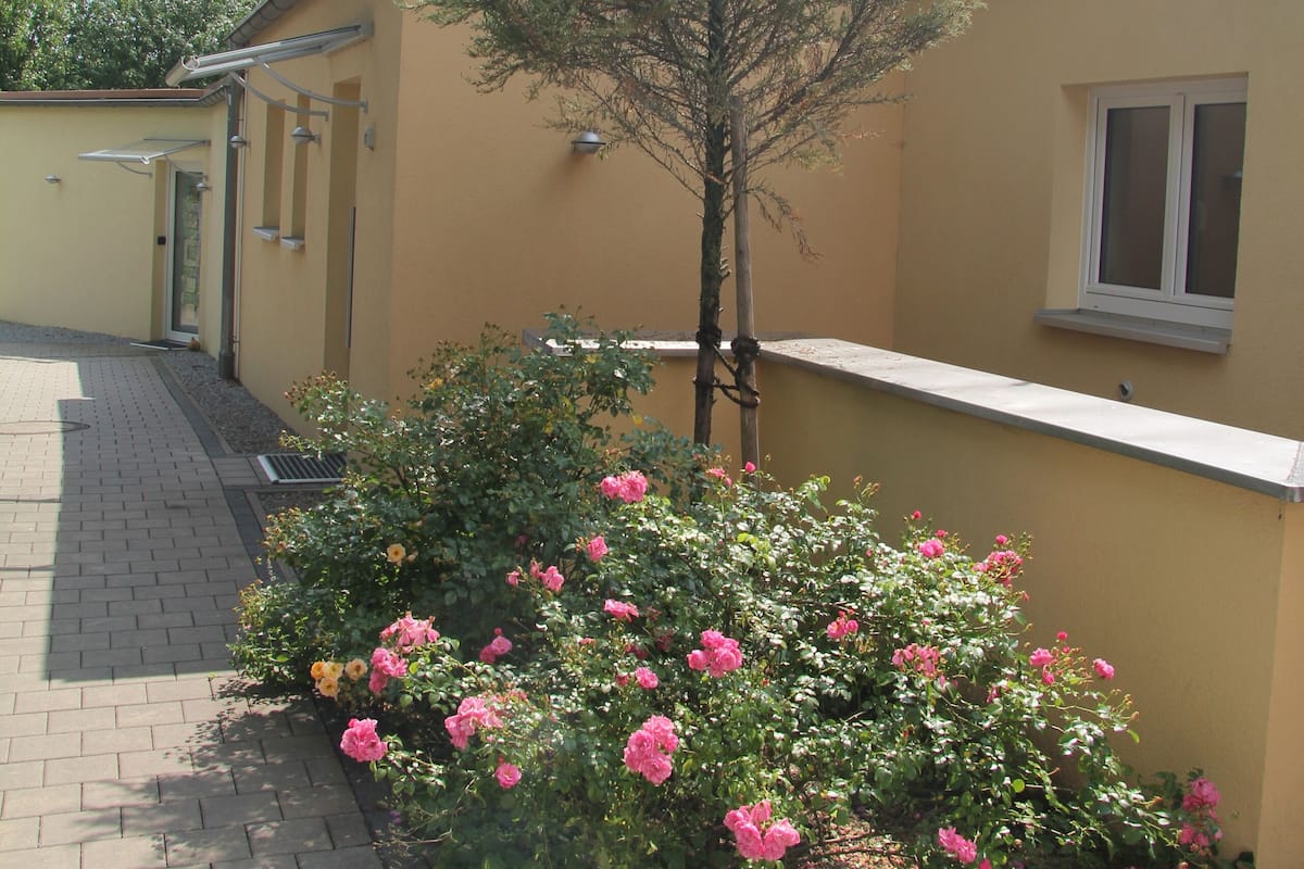 A building with a yellow exterior, a small tree, and pink flowers in the foreground.