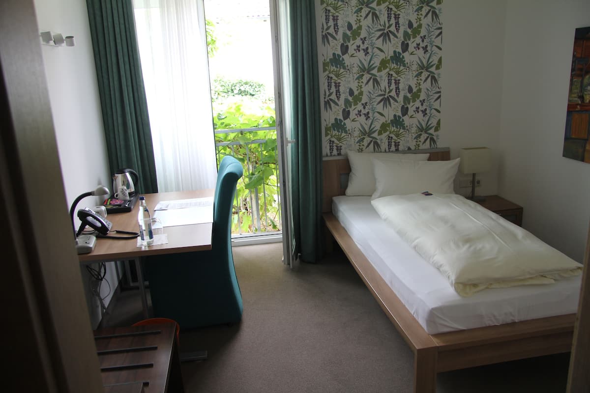 A hotel room with a bed, a desk with a chair, a telephone, and a window with curtains.