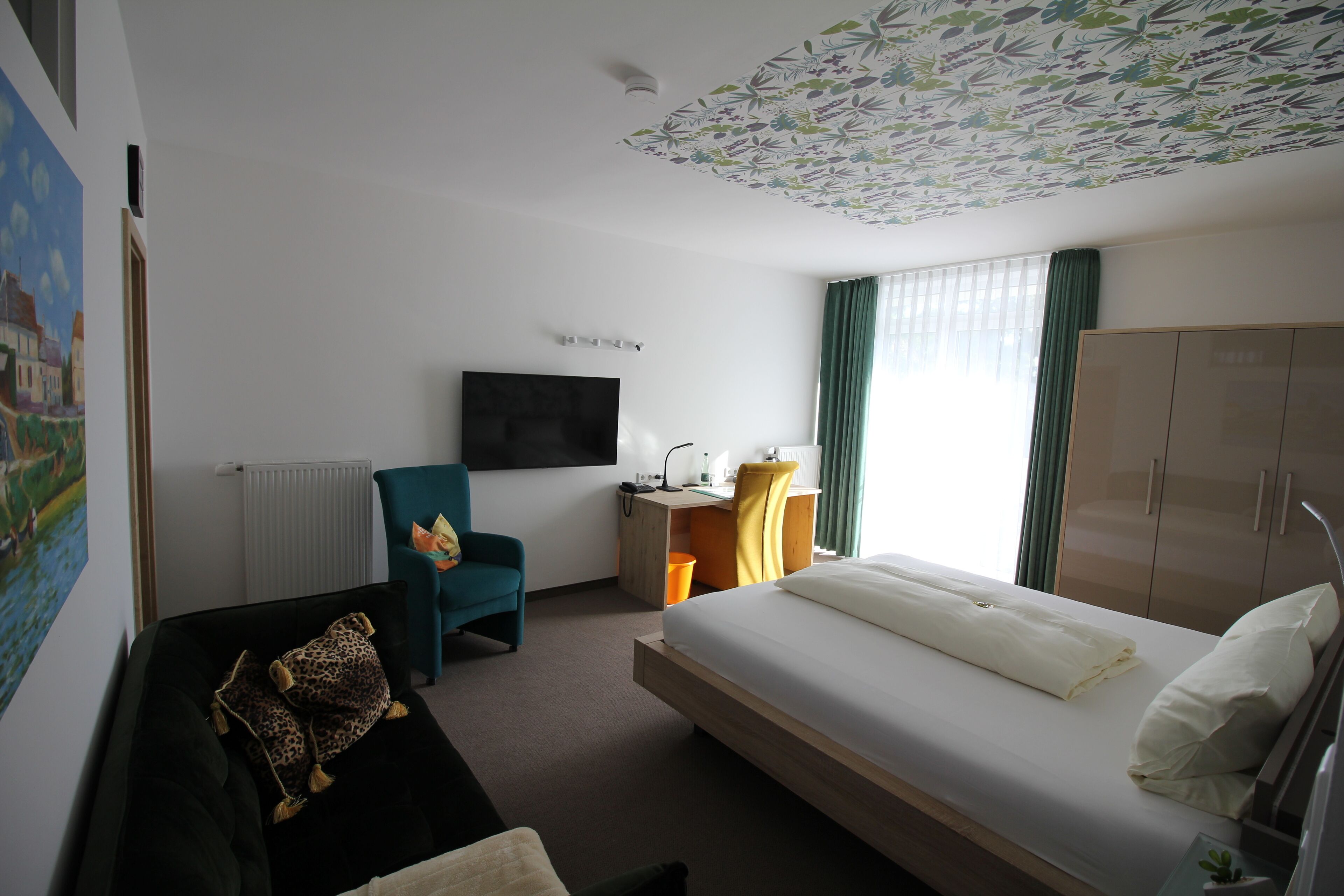 Ein Hotelzimmer mit Bett, Schreibtisch, Stuhl, Fernseher und Kleiderschrank.