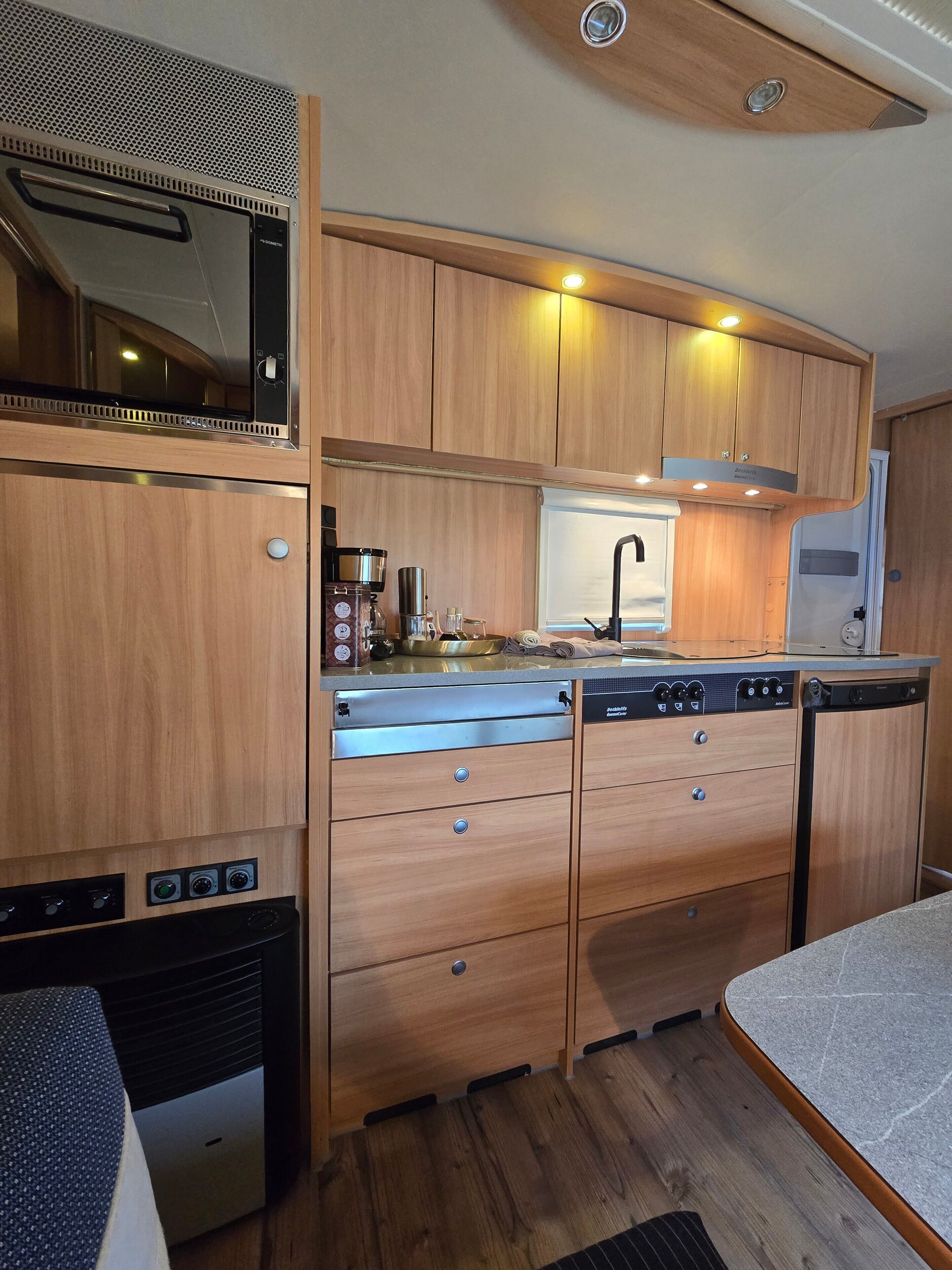 A compact kitchen with wooden cabinets, a built-in microwave, and a coffee maker.