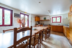 A kitchen with wooden cabinets, a dining table with chairs, and a window with red frames. - Gîte 'Les Carlines' with Mountain View, Shared Terrace and Wi-Fi (Vassieux-en-Vercors)