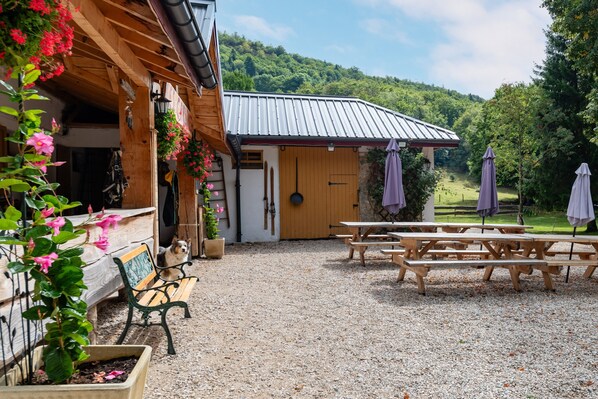 A rustic wooden building with a gravel patio, wooden benches, and picnic tables.