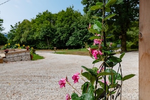 A gravel path leading to a wooden structure, surrounded by greenery and a stone wall.