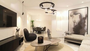 A modern living room with a flat-screen TV, a round coffee table, a sofa, and a dining area in the background. - Al Yassmine 5-6 Apartment - A True Gem (Sfax)