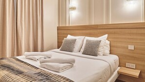 A neatly made bed with white linens and a folded towel, a wooden headboard, and two wall-mounted light fixtures. - Superb air-conditioned flat on the Champs Elysées (Paris)