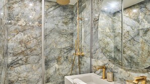 A bathroom with marble walls, a glass-enclosed shower, and a white sink with gold fixtures. - Superb air-conditioned flat on the Champs Elysées (Paris)