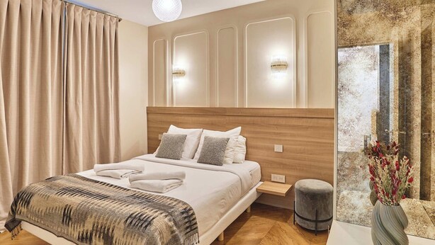 A modern bedroom with a wooden headboard, a large bed with white linens, a bedside table, and a small stool. - Superb air-conditioned flat on the Champs Elysées (Paris)
