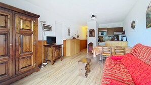 A living room with a wooden cabinet, a television, a sofa, and a dining area with a table and chairs. - Isabella IS65 VIEW & CENTER 4 Pers. (Châtel)