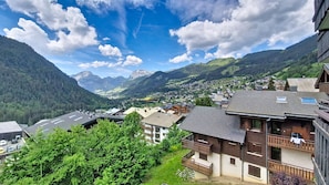 A mountain village with traditional wooden houses, a valley, and distant mountains.