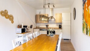 Eine moderne Küche mit Holzschränken, einer Edelstahl-Dunstabzugshaube und einem Essbereich mit Holztisch und weißen Stühlen.