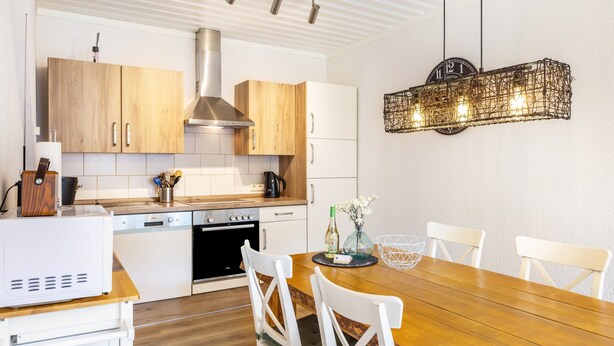 Eine moderne Küche mit Holzschränken, einer Edelstahl-Dunstabzugshaube und einem Essbereich mit Holztisch und weißen Stühlen.