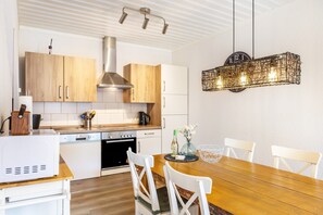 A modern kitchen with wooden cabinets, a stainless steel range hood, and a dining area with a wooden table and white chairs. - Apartment 'Sonnentraum' with Mountain View, Shared Terrace and Wi-Fi (Willingen (Upland))