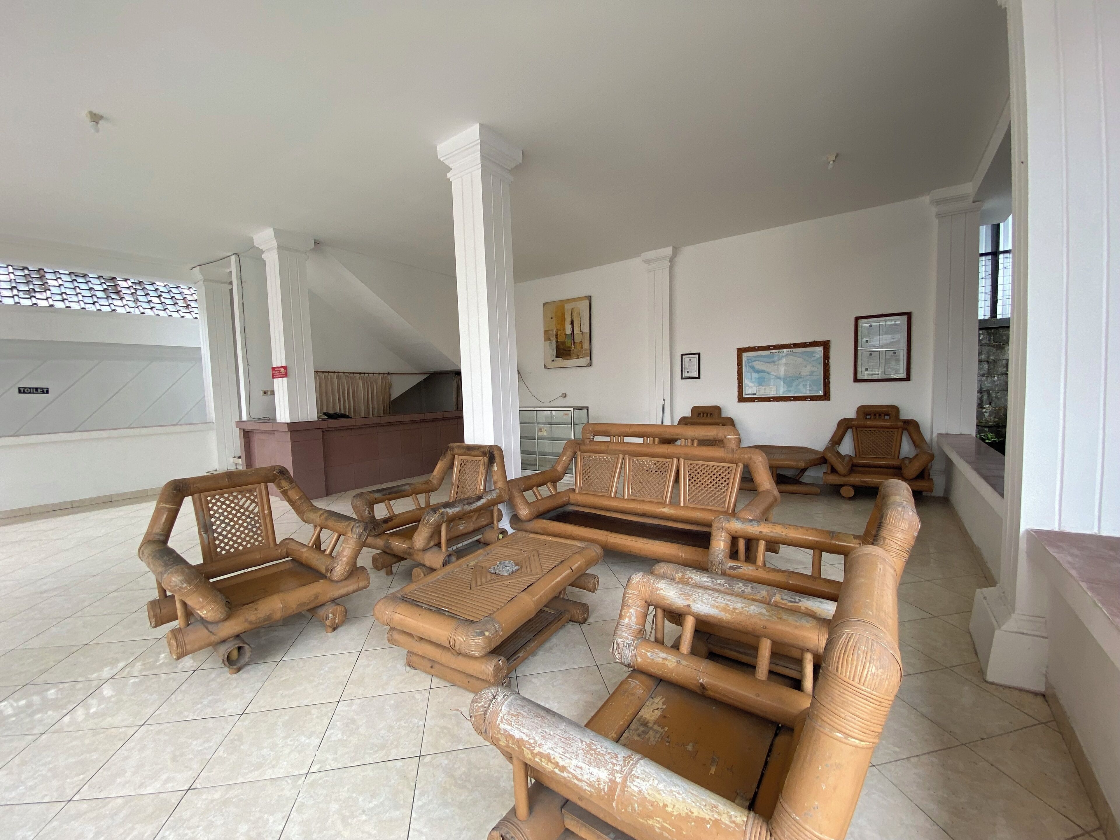 A spacious room with a large sectional sofa, a small table, and a bench. There is a sign indicating a toilet nearby.