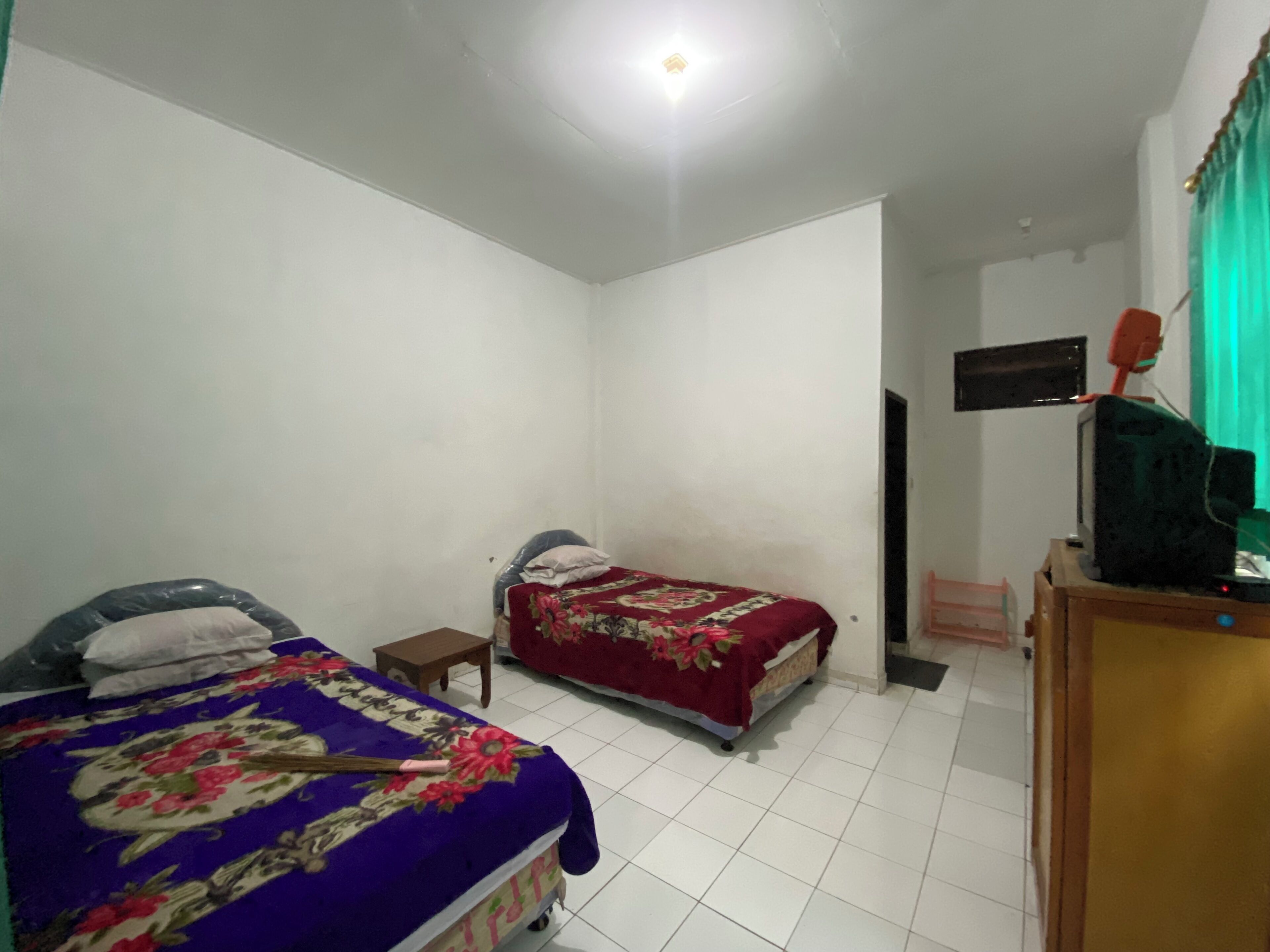 A bedroom with two single beds, a small table, a TV on a wooden stand, and a green curtain.