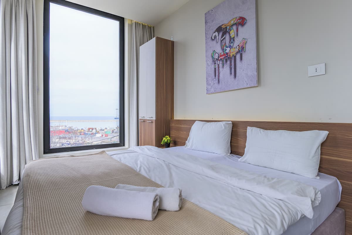 A hotel room with a large bed, a view of the city, and a painting on the wall.