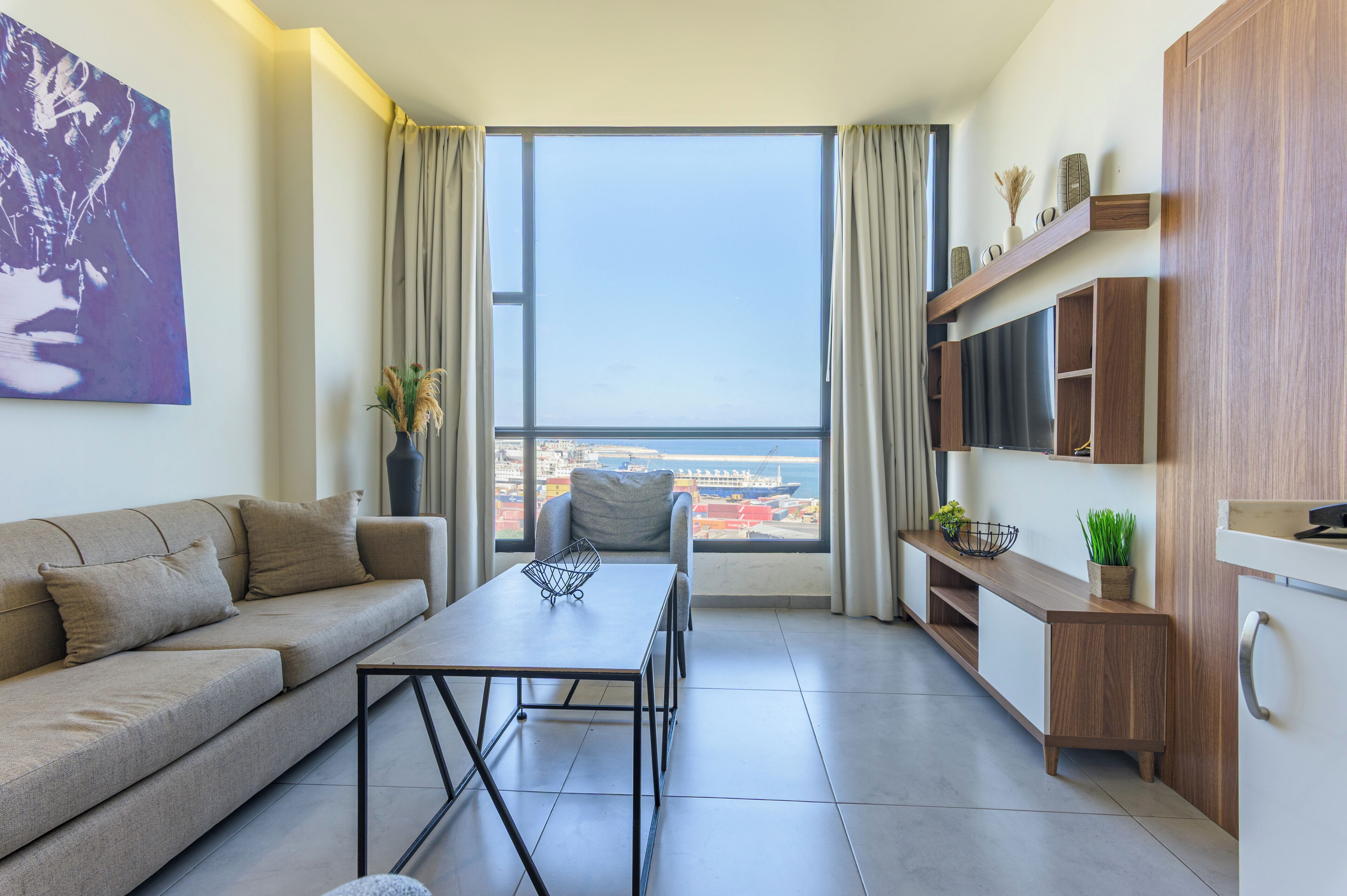 A modern living room with a sofa, a dining table, and a view of the sea through large windows.