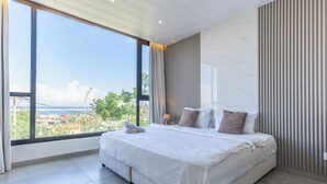 Un dormitorio moderno con un ventanal grande, una cama con sábanas blancas y vistas a un paisaje urbano.