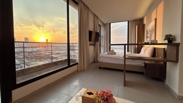 Habitación de hotel con cama, escritorio, ventana grande con vistas a la ciudad, planta y reloj.