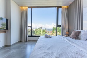 A modern hotel room with a large window, a bed with white linens, a flat-screen TV on a wooden shelf, and a lamp on a bedside table. - Gate 9 Tower -Studios & Apts Mar Mikhael (Beirut)
