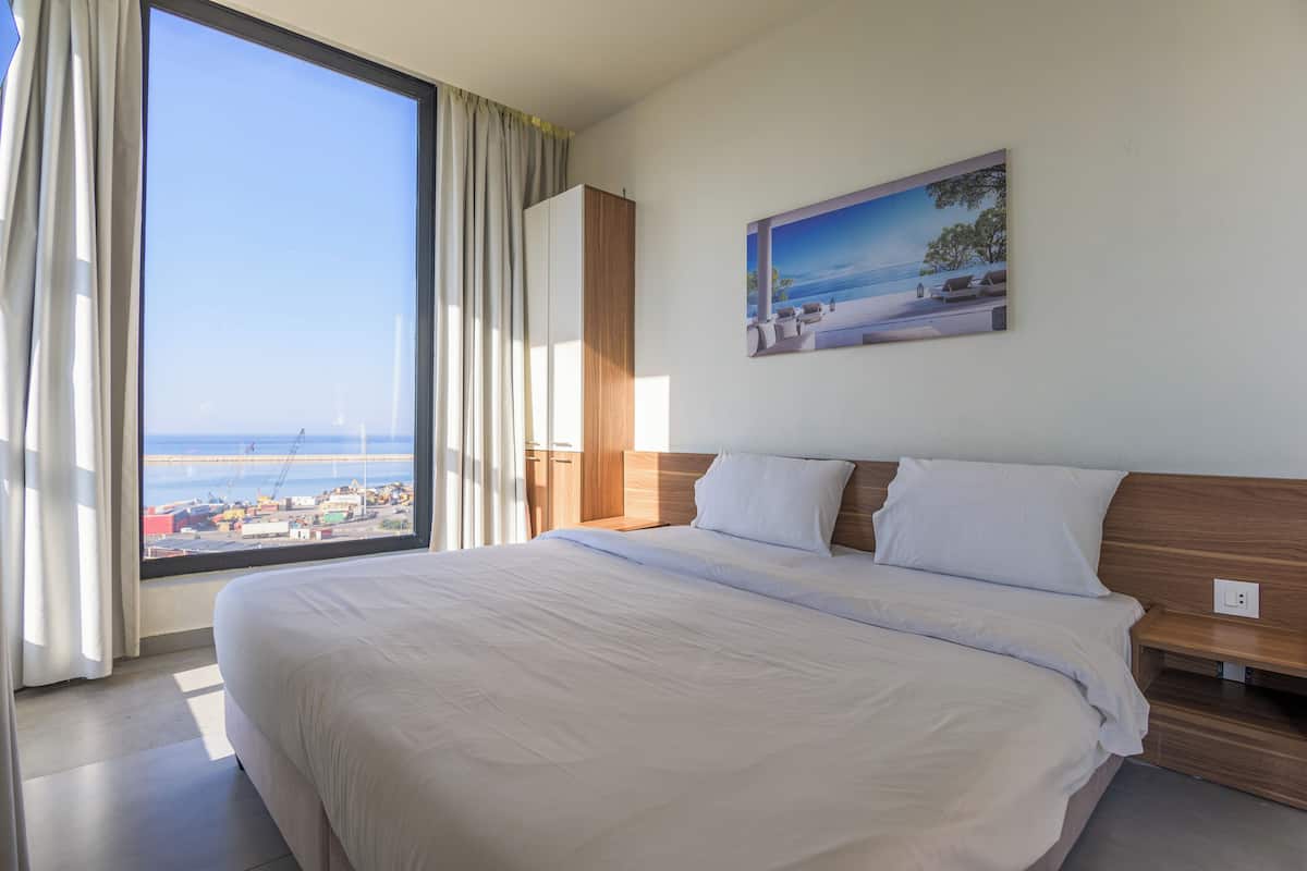 A hotel room with a large bed, a wooden headboard, a nightstand, and a painting of a beach scene.