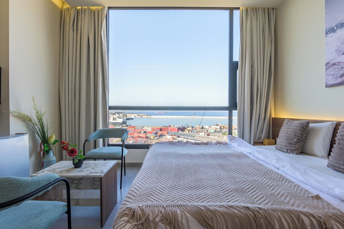 A hotel room with a large window, a bed, a desk, and a chair.