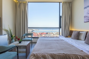 A hotel room with a large window, a bed, a desk, and a chair. - Gate 9 Tower -Studios & Apts Mar Mikhael (Beirut)