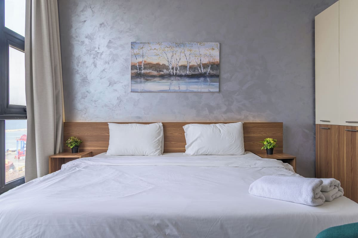 A neatly made bed with white linens, a wooden headboard, and two bedside tables with small potted plants.