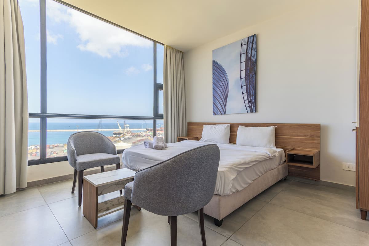 A hotel room with a large window, a bed, a desk, and a chair.