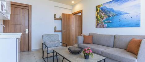 A modern living room with a grey sofa, a coffee table, and a painting of a coastal scene.