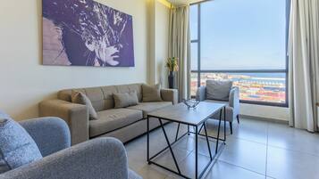 A modern living room with a sofa, armchairs, a coffee table, and a large window offering a city view.