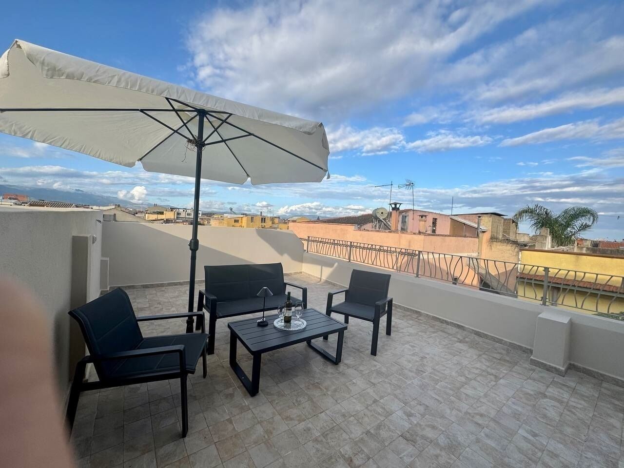 A rooftop terrace with two black chairs, a small table, and a white umbrella.