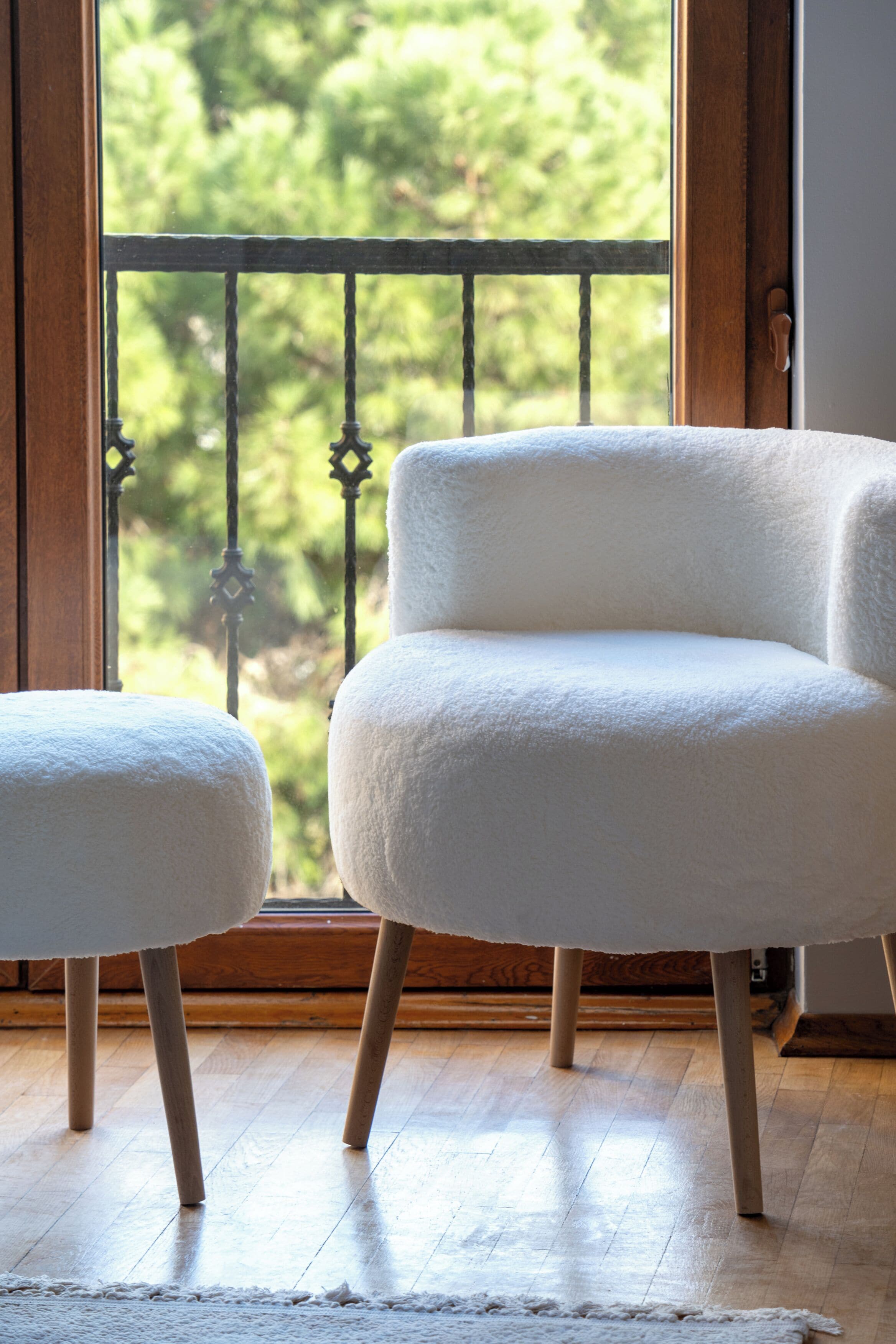 Una habitación con piso de madera, una silla blanca y un otoman que combina.